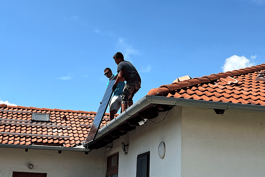Pracovníci přenášejí monoskleněný IBC fotovoltaický modul na střechu rodinného domu k instalaci. Pracovníci přenášejí monoskleněný IBC fotovoltaický modul na střechu rodinného domu k instalaci.