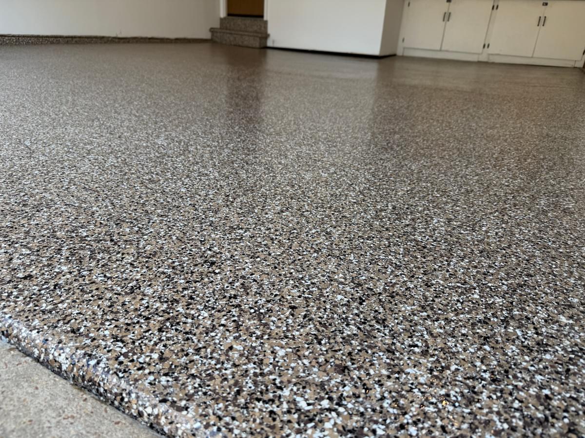 Quality Floor Coatings, a garage floor solutions company in Ellisville, MO, showcasing a garage floor makeover. The image shows a gray and black patterned epoxy floor installed by Quality Floor Coatings. The floor is glossy, smooth, and durable, providing a modern and functional look to the garage. Quality Floor Coatings, a garage floor solutions company in Ellisville, MO, showcasing a garage floor makeover. The image shows a gray and black patterned epoxy floor installed by Quality Floor Coatings. The floor is glossy, smooth, and durable, providing a modern and functional look to the garage.