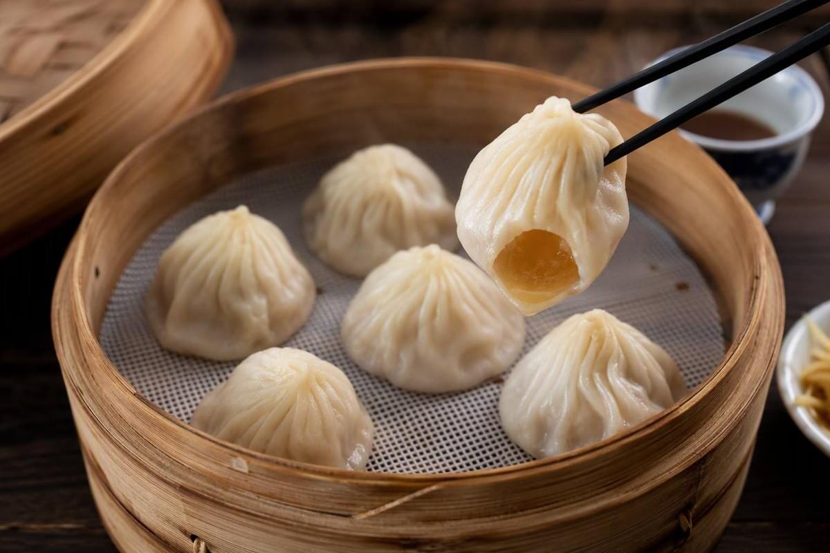 Stacked bamboo steamers of xiao long bao in a bustling dim sum kitchen, steam rising from the freshly opened lid. Stacked bamboo steamers of xiao long bao in a bustling dim sum kitchen, steam rising from the freshly opened lid.