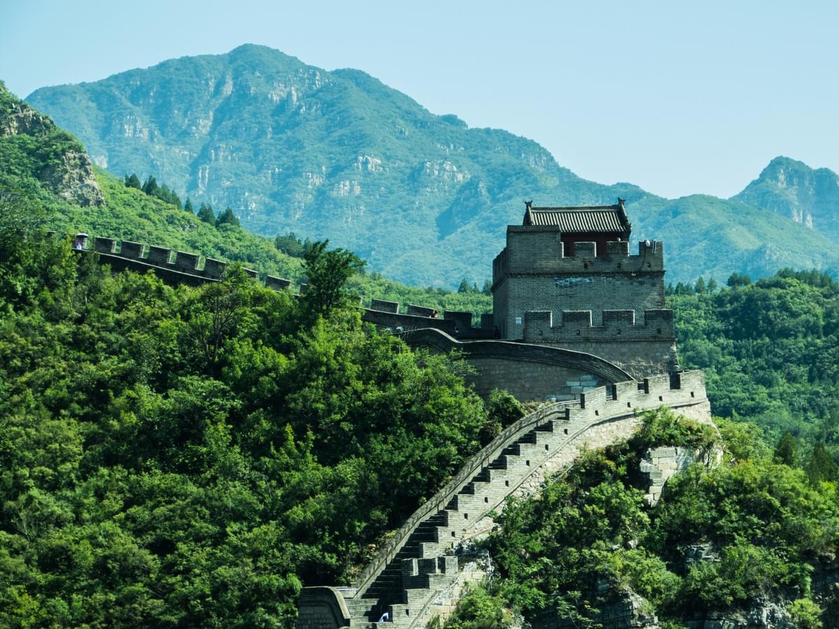 The Great Wall of China winding across lush green mountain ridges under a bright sky The Great Wall of China winding across lush green mountain ridges under a bright sky