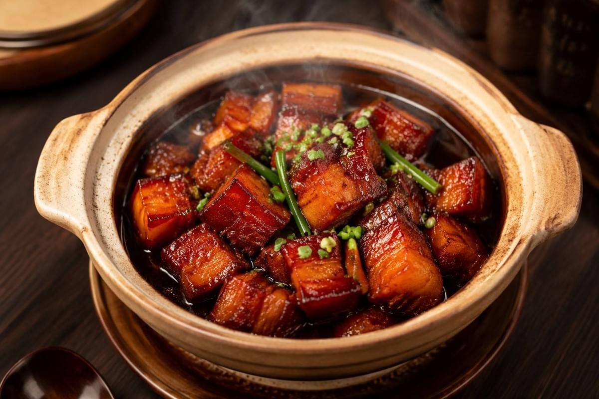 hanghai-style braised pork belly in a traditional clay pot, tender glossy chunks of pork simmered in rich dark soy-based caramelized sauce, garnished with green onion, warm indoor lighting. hanghai-style braised pork belly in a traditional clay pot, tender glossy chunks of pork simmered in rich dark soy-based caramelized sauce, garnished with green onion, warm indoor lighting.