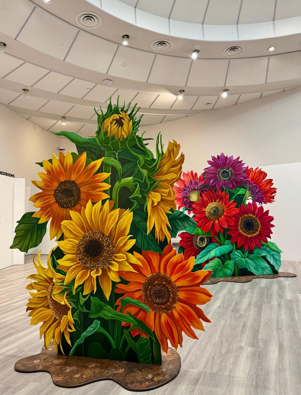 "The Love You Planted" by Ariana Enriquez featuring large hand-cut sunflower paintings installed as sculptural artworks in a gallery space. "The Love You Planted" by Ariana Enriquez featuring large hand-cut sunflower paintings installed as sculptural artworks in a gallery space.