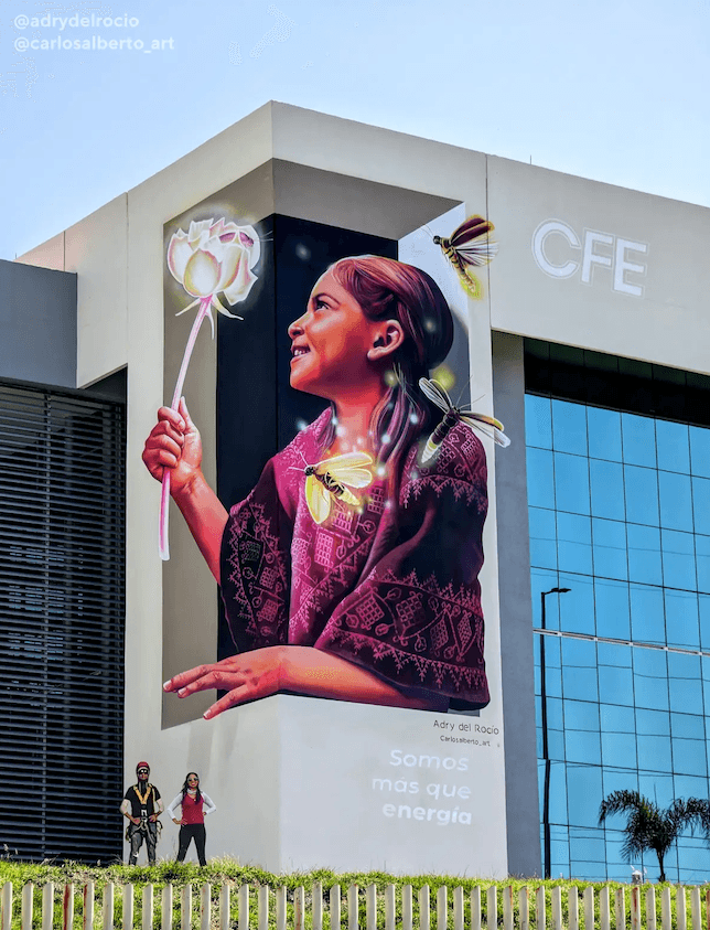Large public mural by Mexican artist Adry del Rocío featuring a smiling young girl holding a glowing flower surrounded by luminous fireflies, symbolizing hope, wonder, and the beauty of childhood. Large public mural by Mexican artist Adry del Rocío featuring a smiling young girl holding a glowing flower surrounded by luminous fireflies, symbolizing hope, wonder, and the beauty of childhood.