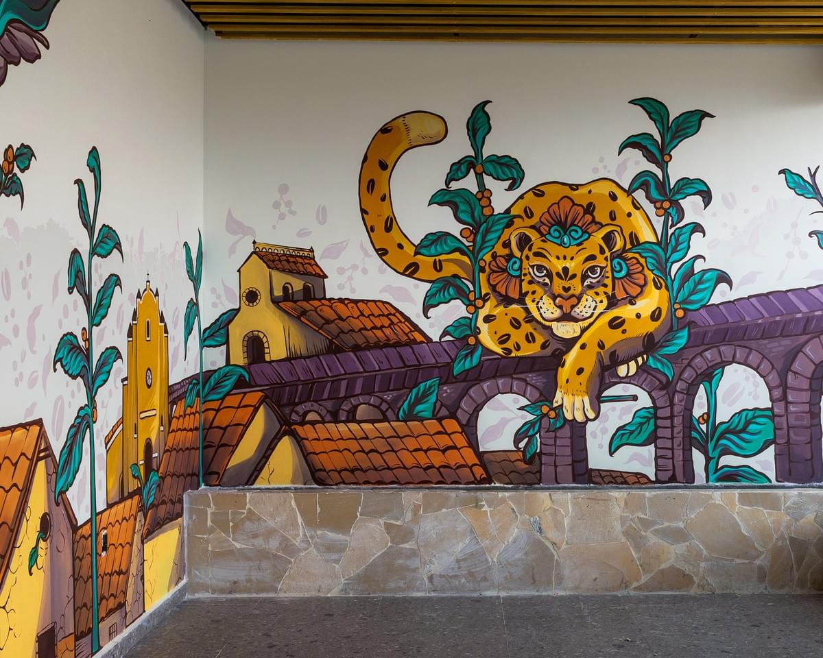 Colorful mural by Miguel Castillo featuring a stylized jaguar surrounded by tropical plants and traditional Mexican architecture inspired by nature and coastal culture. Colorful mural by Miguel Castillo featuring a stylized jaguar surrounded by tropical plants and traditional Mexican architecture inspired by nature and coastal culture.