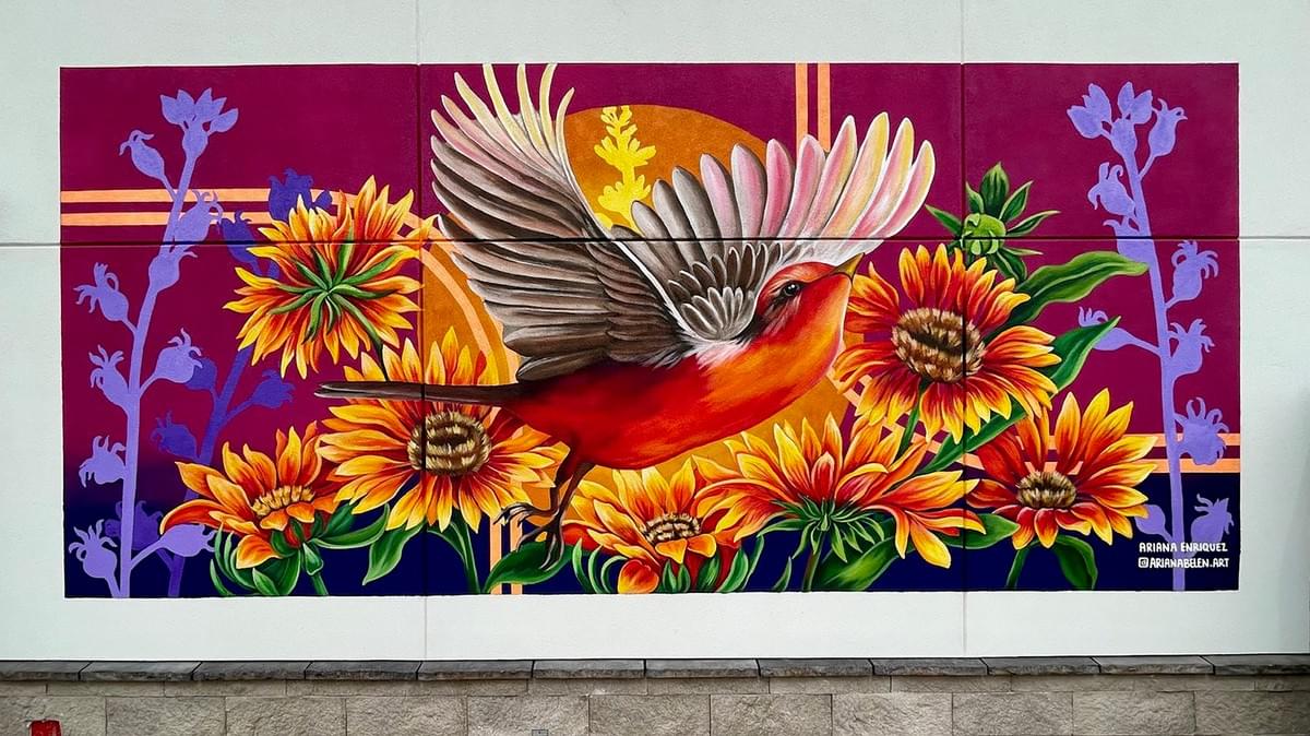 Colorful mural by Ariana Enriquez featuring a vermilion flycatcher in flight surrounded by vibrant Arizona wildflowers and desert plants. Colorful mural by Ariana Enriquez featuring a vermilion flycatcher in flight surrounded by vibrant Arizona wildflowers and desert plants.
