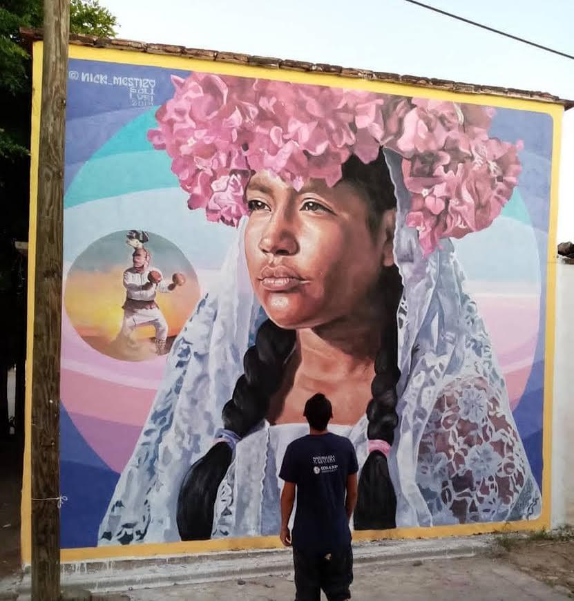 Mural by Mexican artist Nick Mestizo depicting an Indigenous woman wearing a floral headdress and traditional clothing, honoring cultural heritage, identity, and community traditions. Mural by Mexican artist Nick Mestizo depicting an Indigenous woman wearing a floral headdress and traditional clothing, honoring cultural heritage, identity, and community traditions.