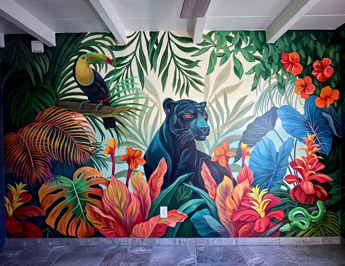 Large mural by Ariana Enriquez featuring a black jaguar, toucan, tropical plants, and vibrant flowers in a colorful rainforest-inspired scene. Large mural by Ariana Enriquez featuring a black jaguar, toucan, tropical plants, and vibrant flowers in a colorful rainforest-inspired scene.