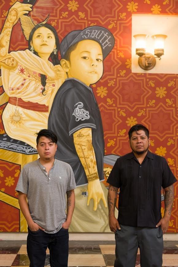 Portrait of the Mexican artist collective Tlacolulokos standing in front of one of their large scale contemporary artworks exploring Indigenous identity and urban culture Portrait of the Mexican artist collective Tlacolulokos standing in front of one of their large scale contemporary artworks exploring Indigenous identity and urban culture