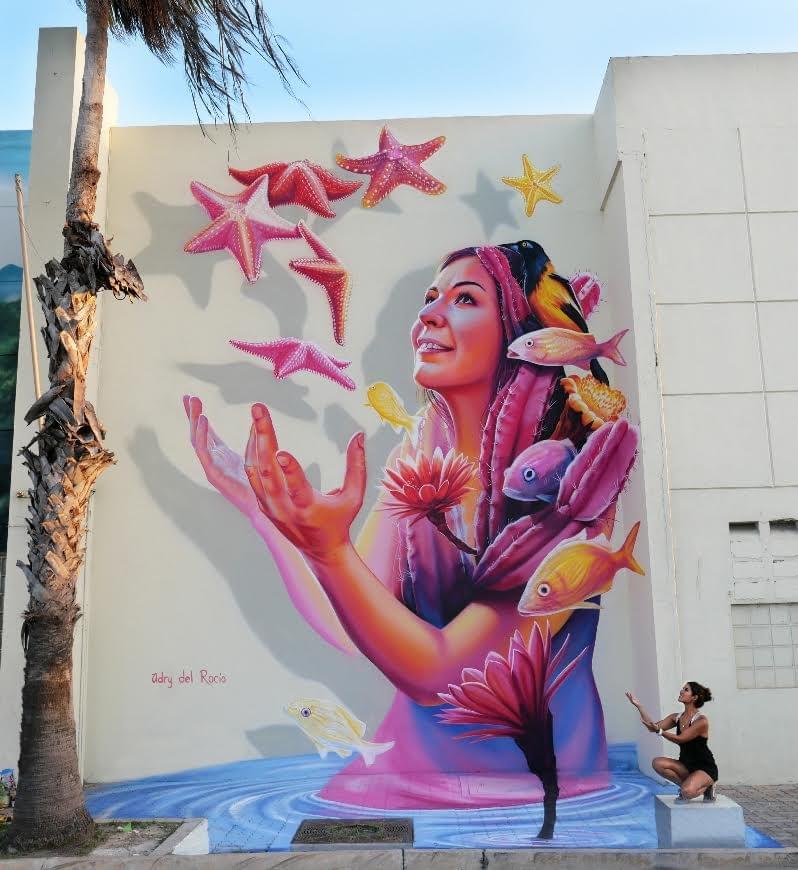 Large mural by Mexican artist Adry del Rocío featuring a woman surrounded by colorful fish, starfish, flowers, and marine life in a surreal underwater-inspired scene. Large mural by Mexican artist Adry del Rocío featuring a woman surrounded by colorful fish, starfish, flowers, and marine life in a surreal underwater-inspired scene.