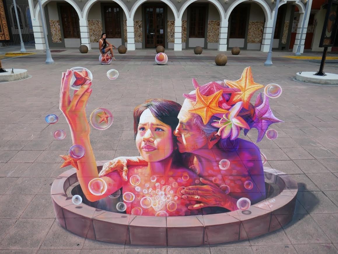 Large 3D chalk artwork by Mexican artist Adry del Rocío depicting a grandmother embracing her granddaughter in an immersive public art installation celebrating family, memory, and love. Large 3D chalk artwork by Mexican artist Adry del Rocío depicting a grandmother embracing her granddaughter in an immersive public art installation celebrating family, memory, and love.