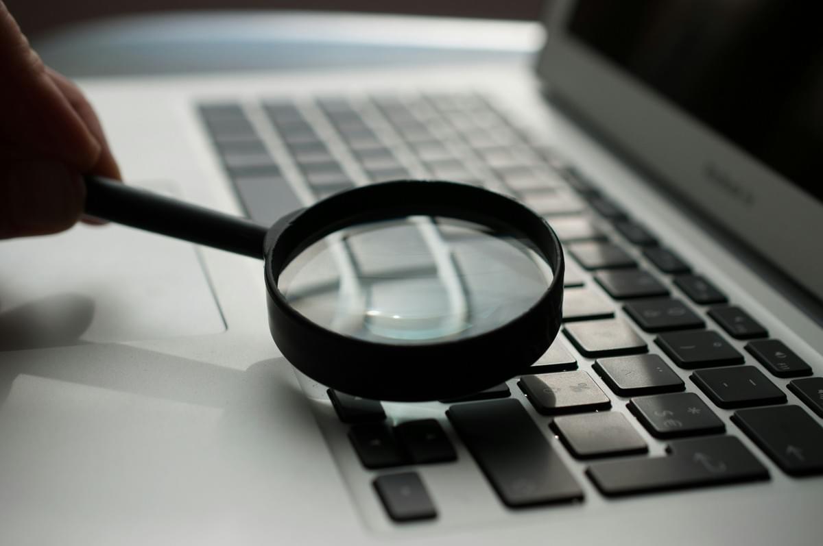 A magnifying glass held above a laptop during an online search review A magnifying glass held above a laptop during an online search review