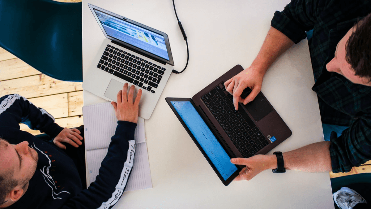Two colleagues review digital work together on separate laptops Two colleagues review digital work together on separate laptops