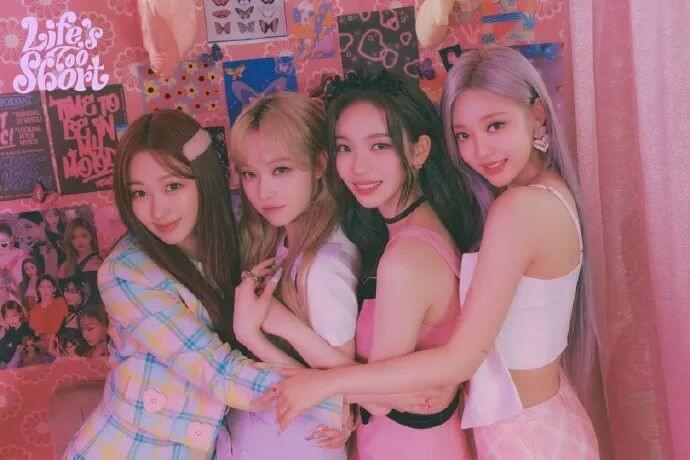 The four members of aespa embracing against a pink collage backdrop. The four members of aespa embracing against a pink collage backdrop.