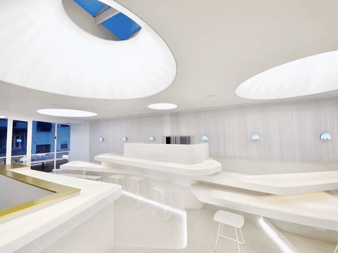 Bright white WE COFFEE interior with curved counters, stools, and oval ceiling lights. Bright white WE COFFEE interior with curved counters, stools, and oval ceiling lights.