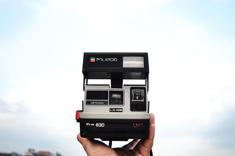 A Polaroid LM 630 camera held up in front of a blue sky with pale clouds A Polaroid LM 630 camera held up in front of a blue sky with pale clouds