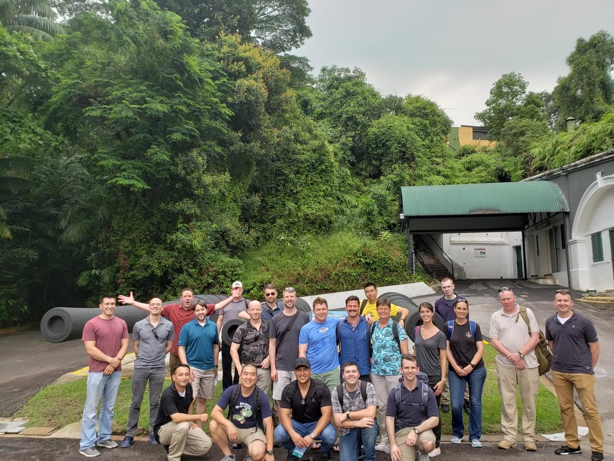 Group of smiling people posting for a photo in front of a large naval canon Group of smiling people posting for a photo in front of a large naval canon