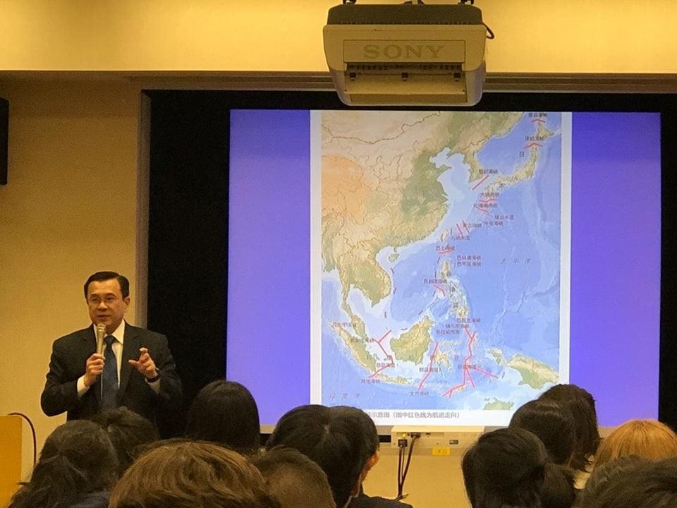 A man in a suit lectures to a seminar room full of people. The projector shows a slide of a map of East and Southeast Asia A man in a suit lectures to a seminar room full of people. The projector shows a slide of a map of East and Southeast Asia