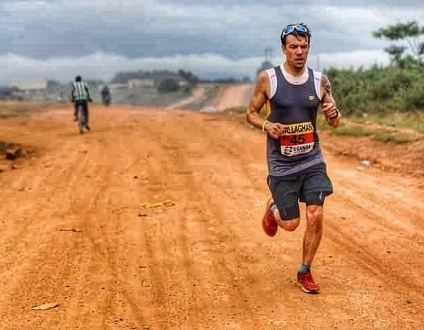 A marathon runner on the red dirt roads of Masaka during the Uganda Marathon, a local man cycles in the background A marathon runner on the red dirt roads of Masaka during the Uganda Marathon, a local man cycles in the background