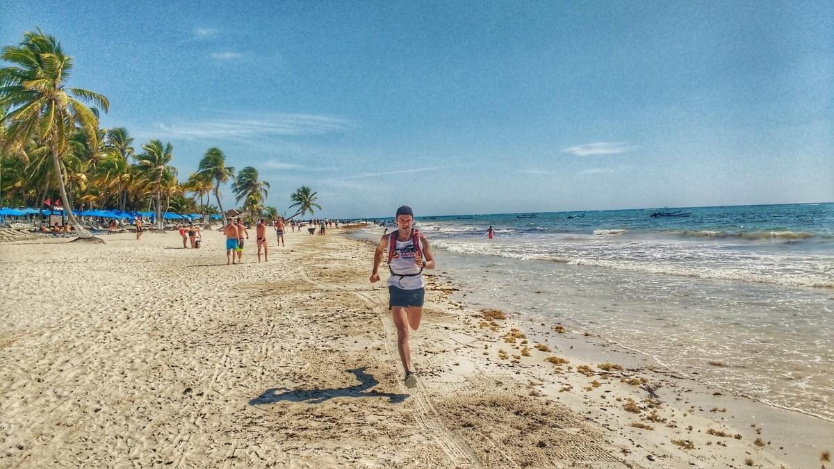 A runner on the beachfront in Tulum, Mexico. Palms and tourists on the left, Caribbean Sea to the right. A runner on the beachfront in Tulum, Mexico. Palms and tourists on the left, Caribbean Sea to the right.