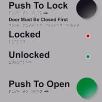 Internal door control panel, with braille and tactile text saying "Push to Lock", "Locked", "Unlocked" and "Push to Open". There is a big black button next to "Push to Lock", a red light next to "Locked" and a green light next to "Unlocked". There is also a big green button next to the "Push to Open" button. There is a braille equivalent below all tactile text.
