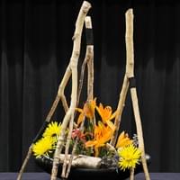 Black ceramic container, white birch branches wrapped in black cord, lilies, chrysanthemums, delphinium, sea holly