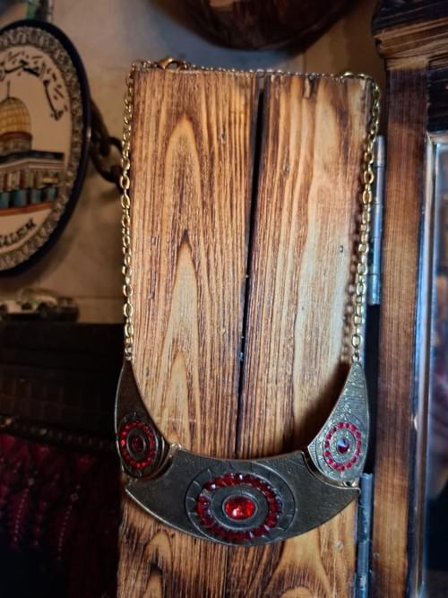 قلادة فنية مميزة بتصميم هندسي مزخرف تتوسطها أحجار حمراء لامعة تضفي فخامة وأناقة استثنائية.