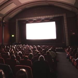 A room full of people watching a screen in the front at a cinema. A room full of people watching a screen in the front at a cinema.