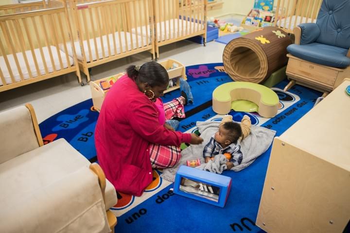 Young girl playing with wooden bead maze toy on floor of child care center