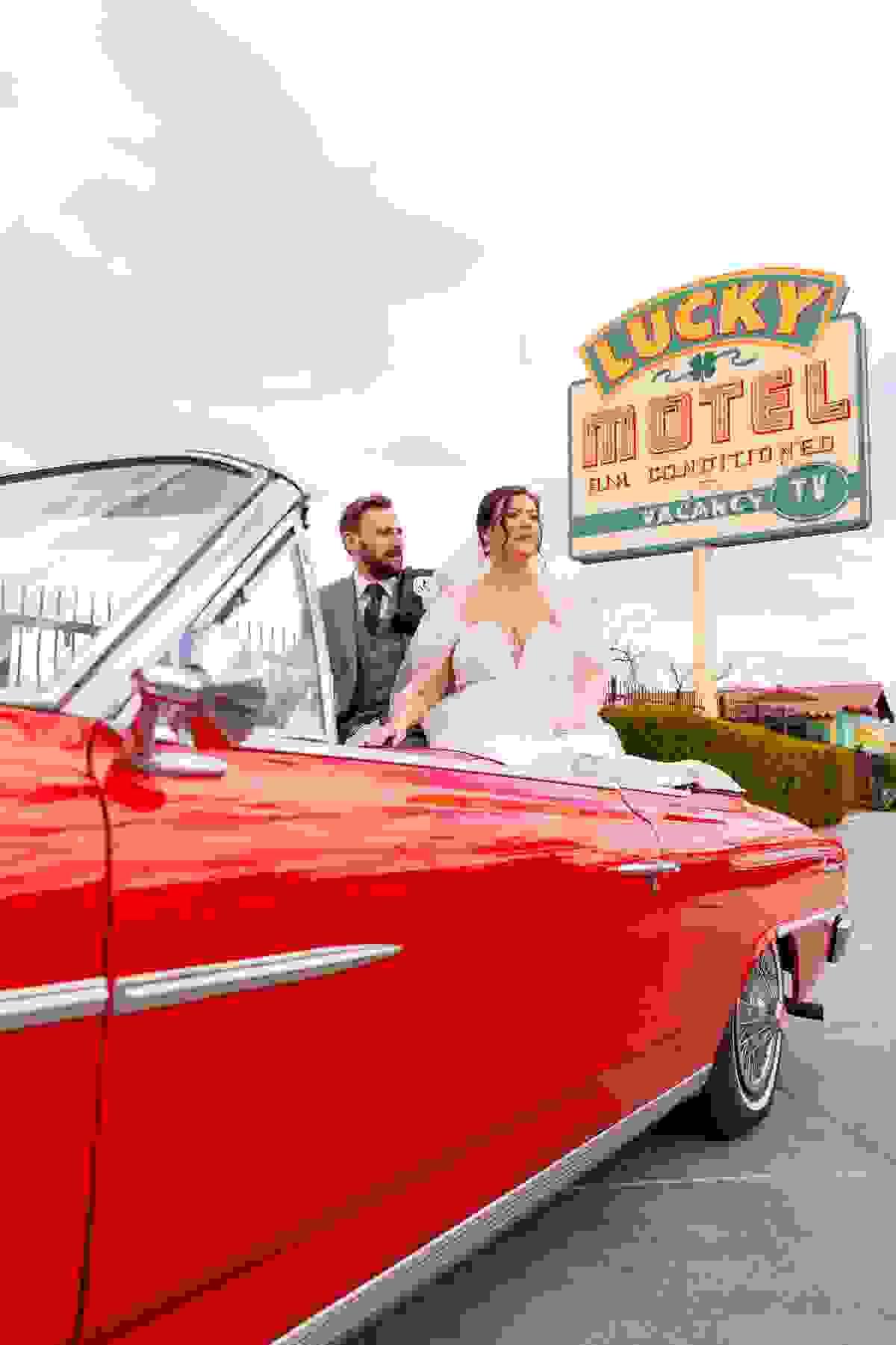 Couple posing next to a red Cadillac on Fremont Street in Las Vegas as part of their Drive Thru wedding experience at Sure Thing Chapel.
