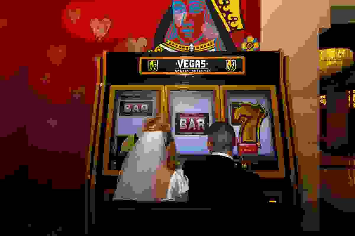 Newlywed couple posing in front of a giant Vegas-themed casino slot machine after their same-day wedding.