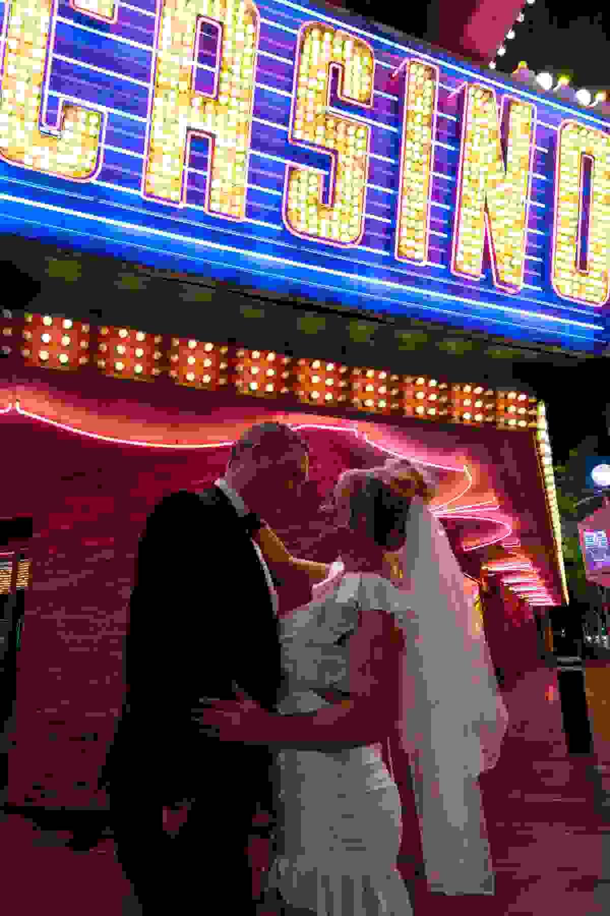 Couple in wedding attire standing under neon lights that say 'Casino' in Las Vegas, captured during their elopement.