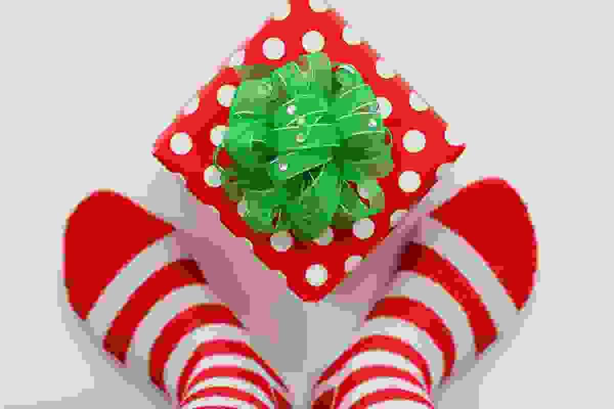 looking down at a box wrapped in red paper with white polka dots and a green bow with little crystals in between two feet wearing striped socks