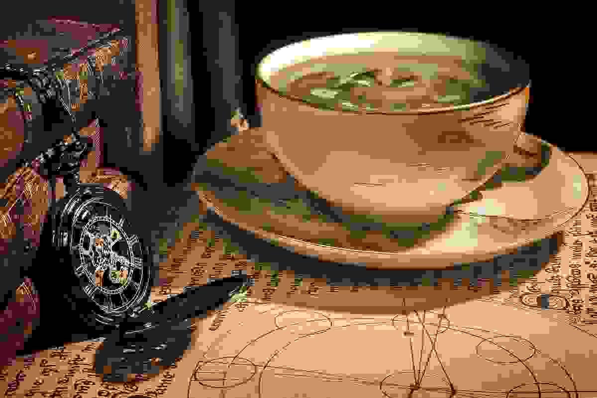 a tea cup on a book and a pocketwatch draped across a stack of books