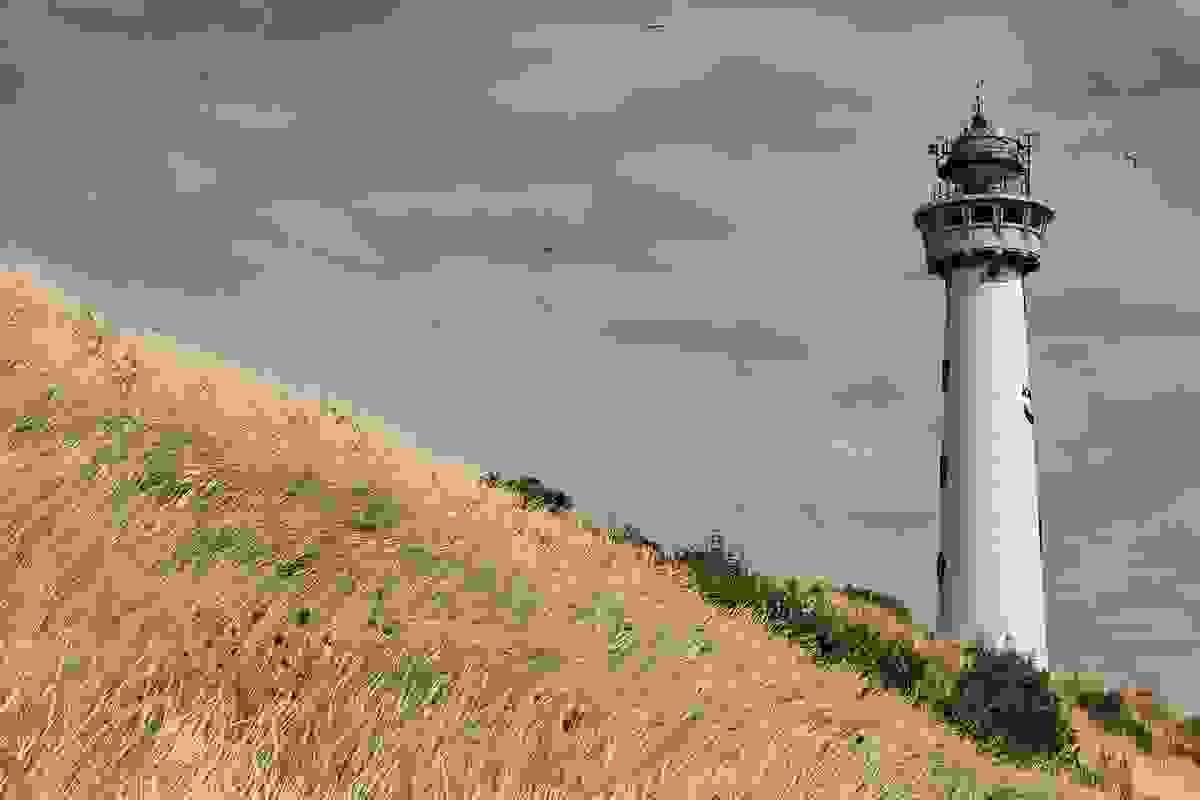 A lighthouse on a hill against a cloudy blue sky
