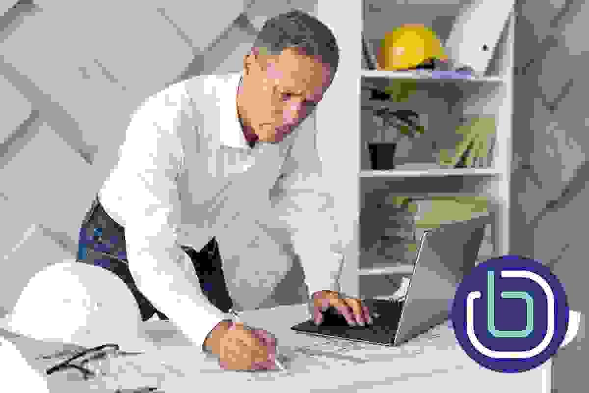 A male architect is looking at a laptop and marking up printed architectural drawings on the desk A male architect is looking at a laptop and marking up printed architectural drawings on the desk