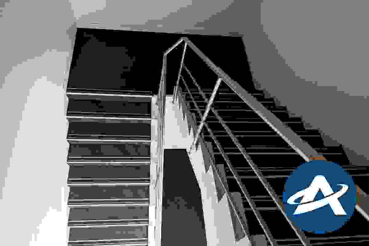 A view looking down a modern stairway with a single stainless steel handrail and non-compliant tread nosing strips (2) A view looking down a modern stairway with a single stainless steel handrail and non-compliant tread nosing strips (2)