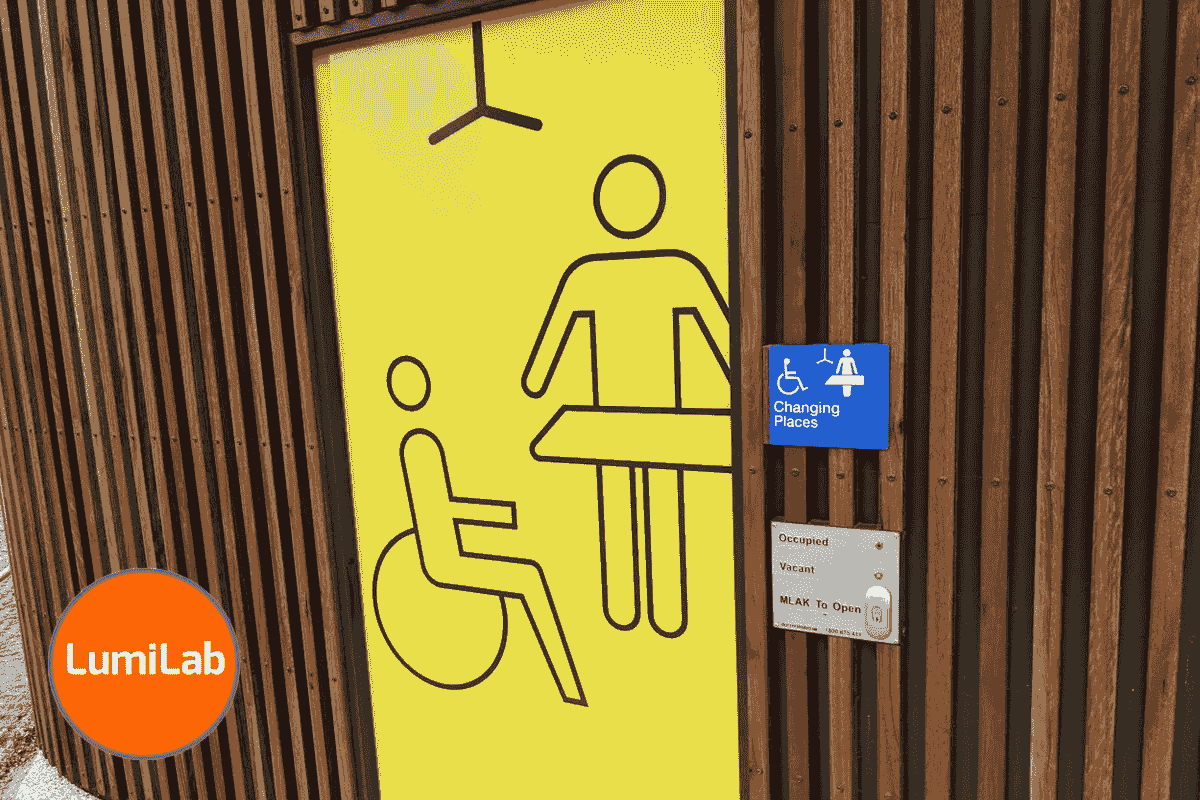 A bright yellow door sign shows a person in a wheelchair and a standing figure beside a changing table, indicating a Changing Places facility, with a blue accessibility sign on the right side of the door. A bright yellow door sign shows a person in a wheelchair and a standing figure beside a changing table, indicating a Changing Places facility, with a blue accessibility sign on the right side of the door.