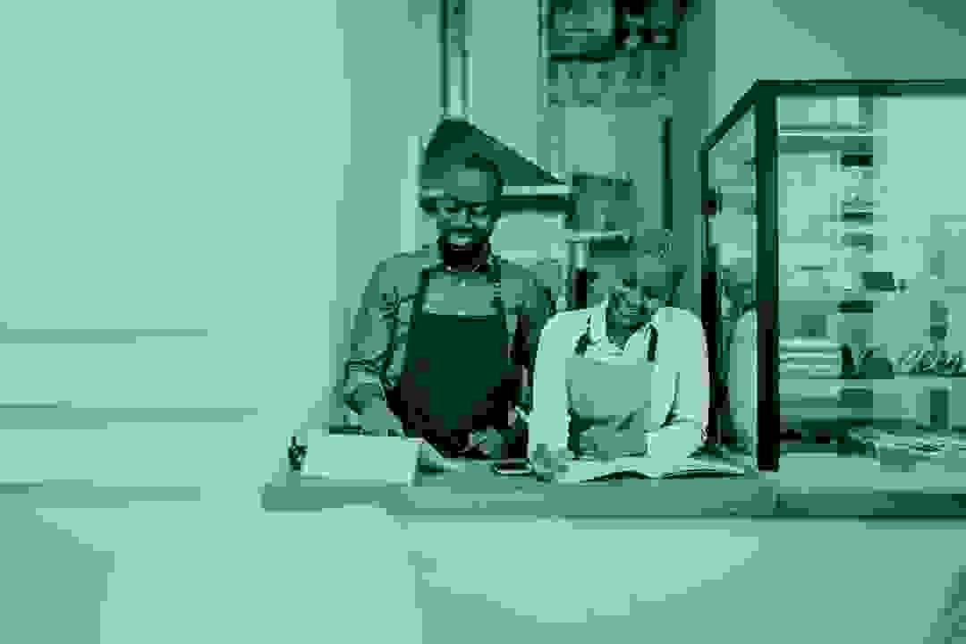 wo small business owners reviewing orders and smiling behind a bakery counter, representing successful startup branding and digital growth wo small business owners reviewing orders and smiling behind a bakery counter, representing successful startup branding and digital growth