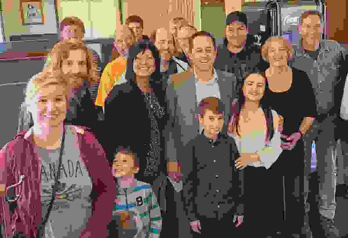 Mark Buzan, sa famille et ses partisans souriants à l'intérieur, rassemblés étroitement pour une photo lors d'un événement.