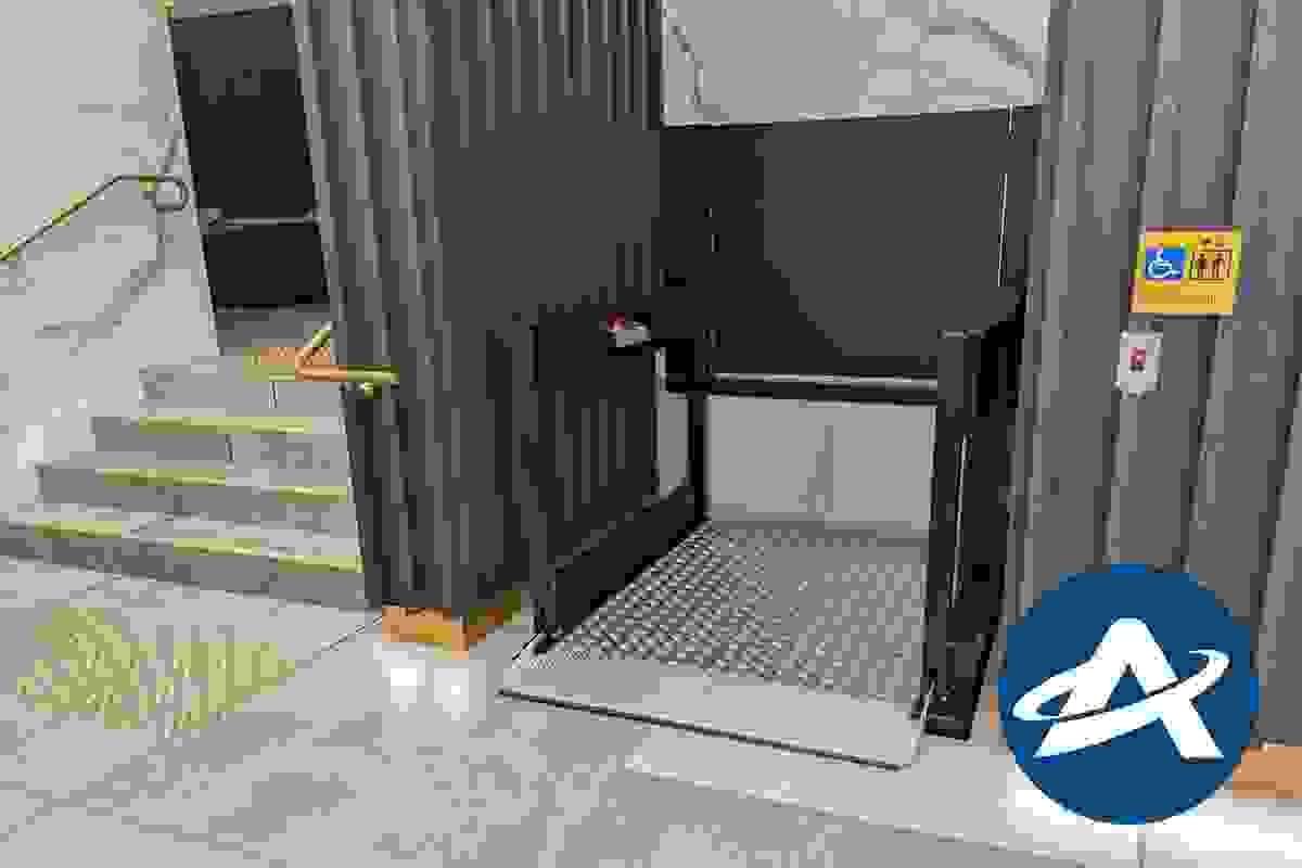 A modern low-rise platform lift is located next to a stairway at the entrance to a building A modern low-rise platform lift is located next to a stairway at the entrance to a building