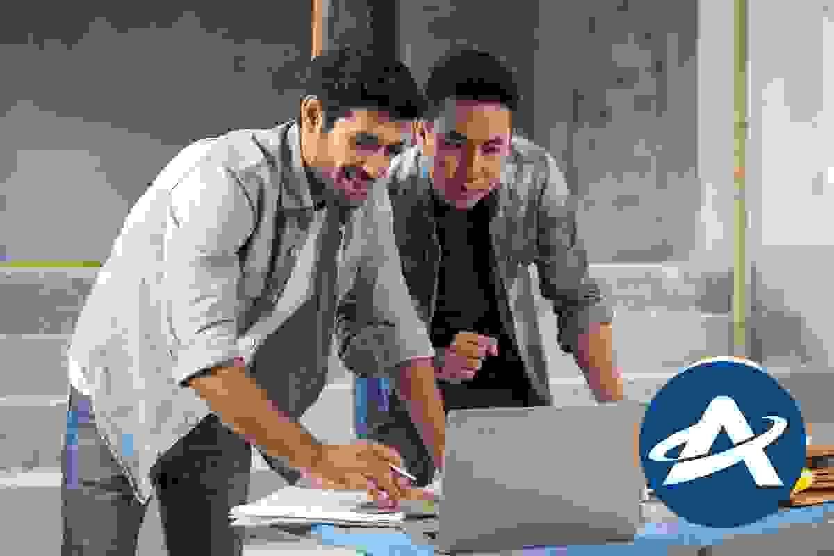 Two men are looking at a laptop on a desk and one is smiling Two men are looking at a laptop on a desk and one is smiling