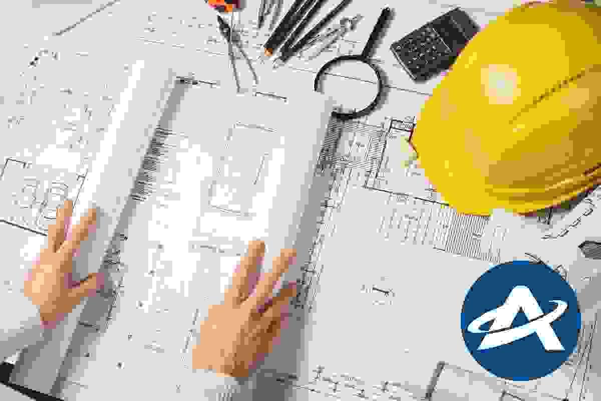 An architect is rolling out architectural drawings onto a design, next to a calculator, pencils and a hardhat An architect is rolling out architectural drawings onto a design, next to a calculator, pencils and a hardhat