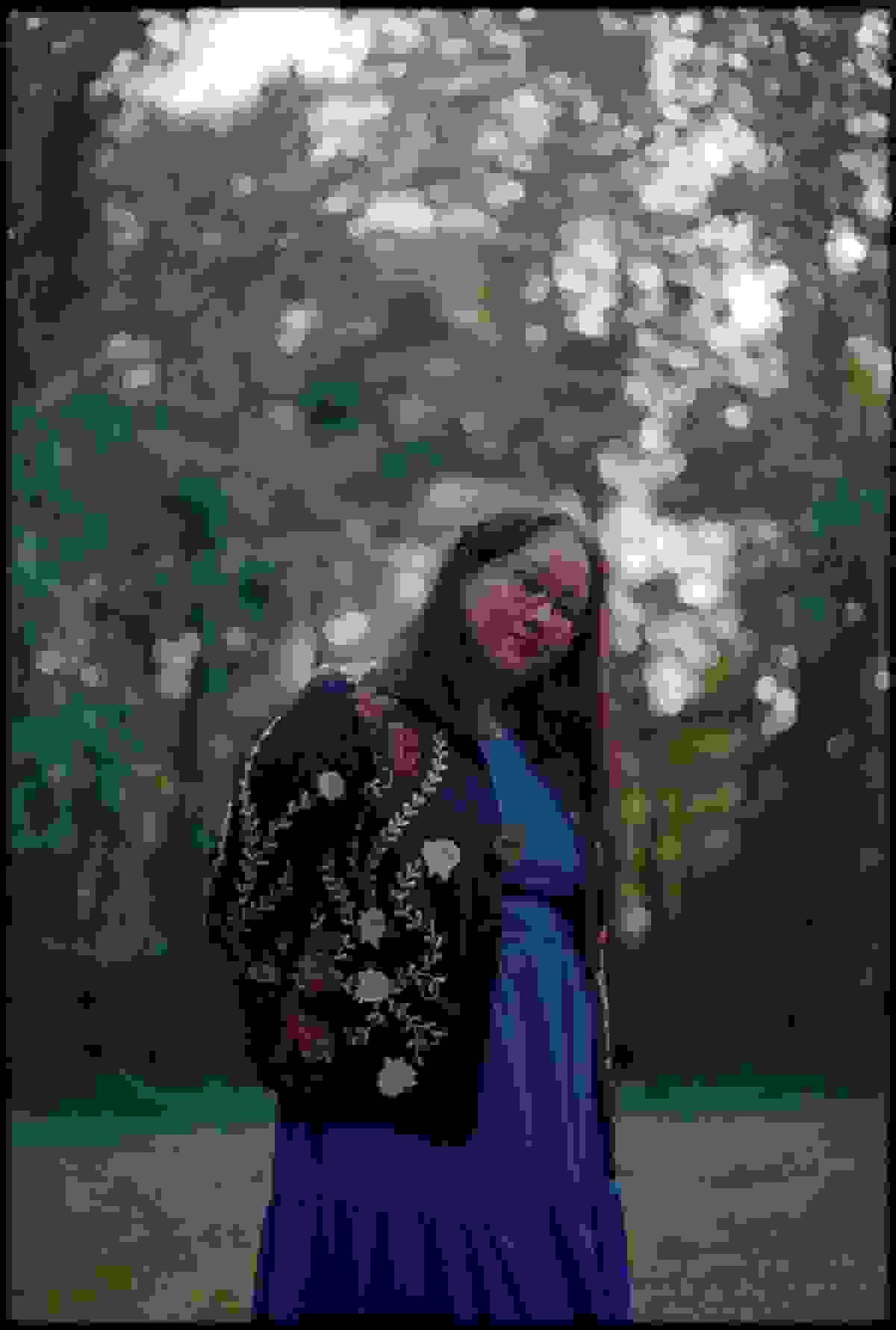 The poet, in a blue dress, standing amid the trees. Photo by Grey Kenna.