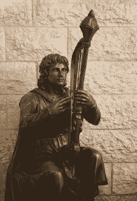 פסל ברונזה של דמות יושבת האוחזת בכלי מיתר, על רקע קיר אבן פסל ברונזה של דמות יושבת האוחזת בכלי מיתר, על רקע קיר אבן