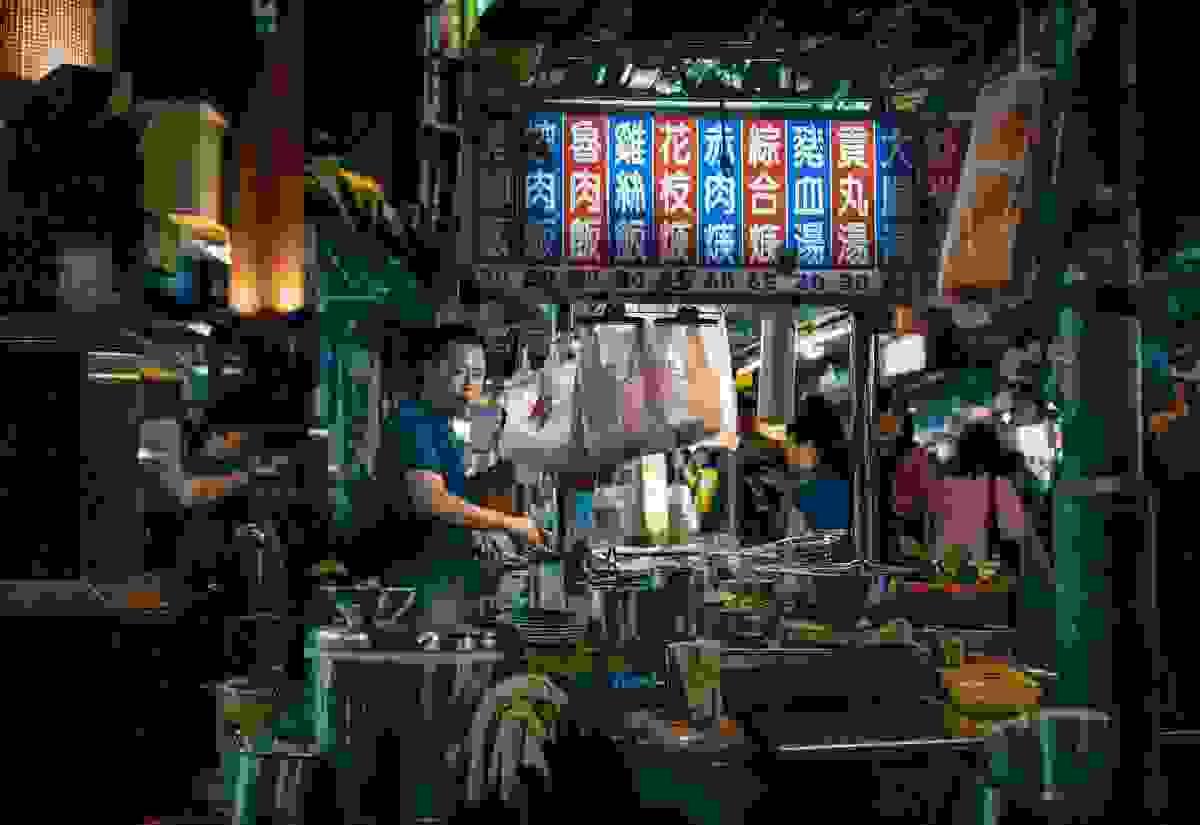 Night market food stall vendor cooking under a neon menu sign with Chinese characters. Night market food stall vendor cooking under a neon menu sign with Chinese characters.