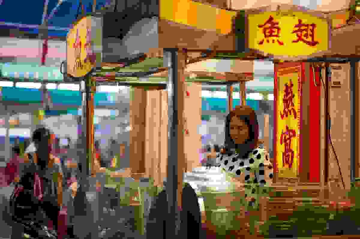 Dedicated hawker stall operator focused on cooking a local dish under bright yellow signage, representing the tradition of Singapore's food culture. Dedicated hawker stall operator focused on cooking a local dish under bright yellow signage, representing the tradition of Singapore's food culture.