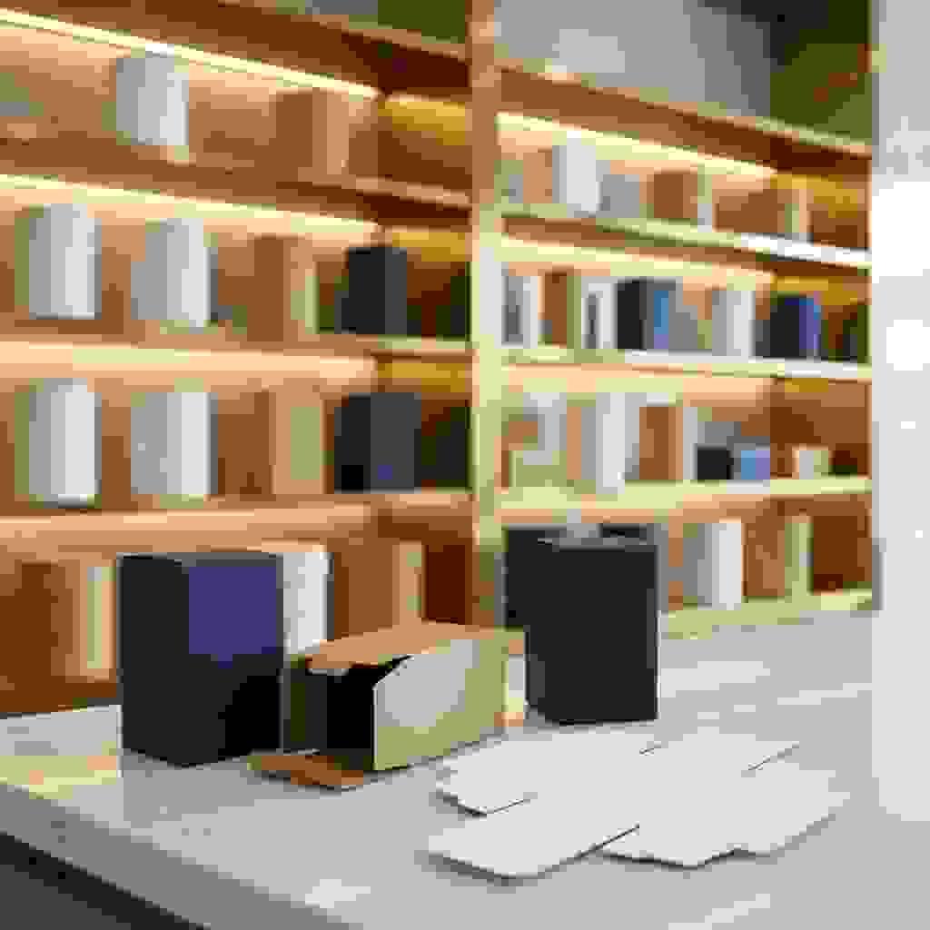 Auto-lock bottom folding carton on marble counter, one open showing reinforced bottom structure, premium showroom. Auto-lock bottom folding carton on marble counter, one open showing reinforced bottom structure, premium showroom.