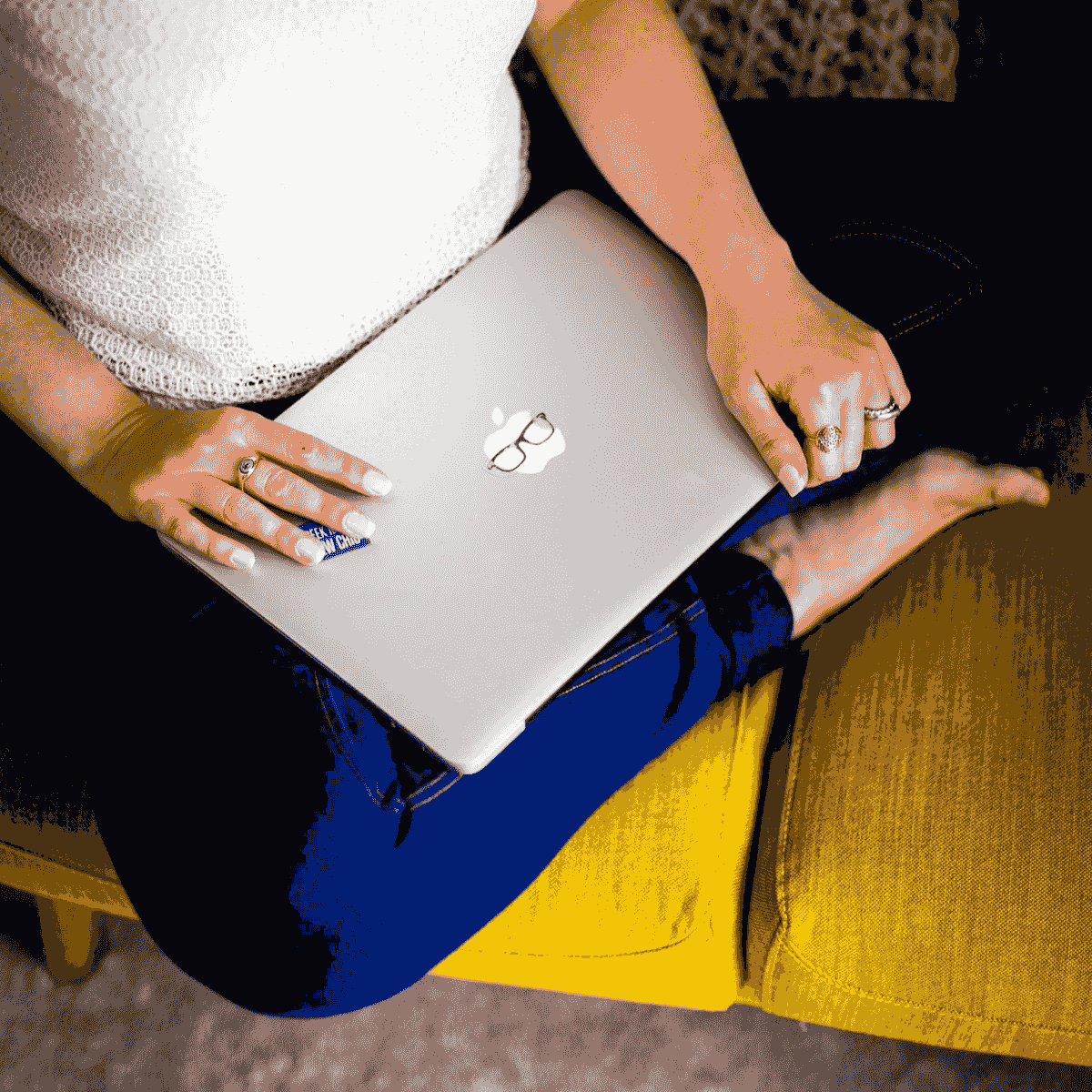 A pregnant woman sits on a mustard coloured sofa wearing leggings. She's holding a laptop preparing to join the Pregnant Pelvis Monthly Workshop.