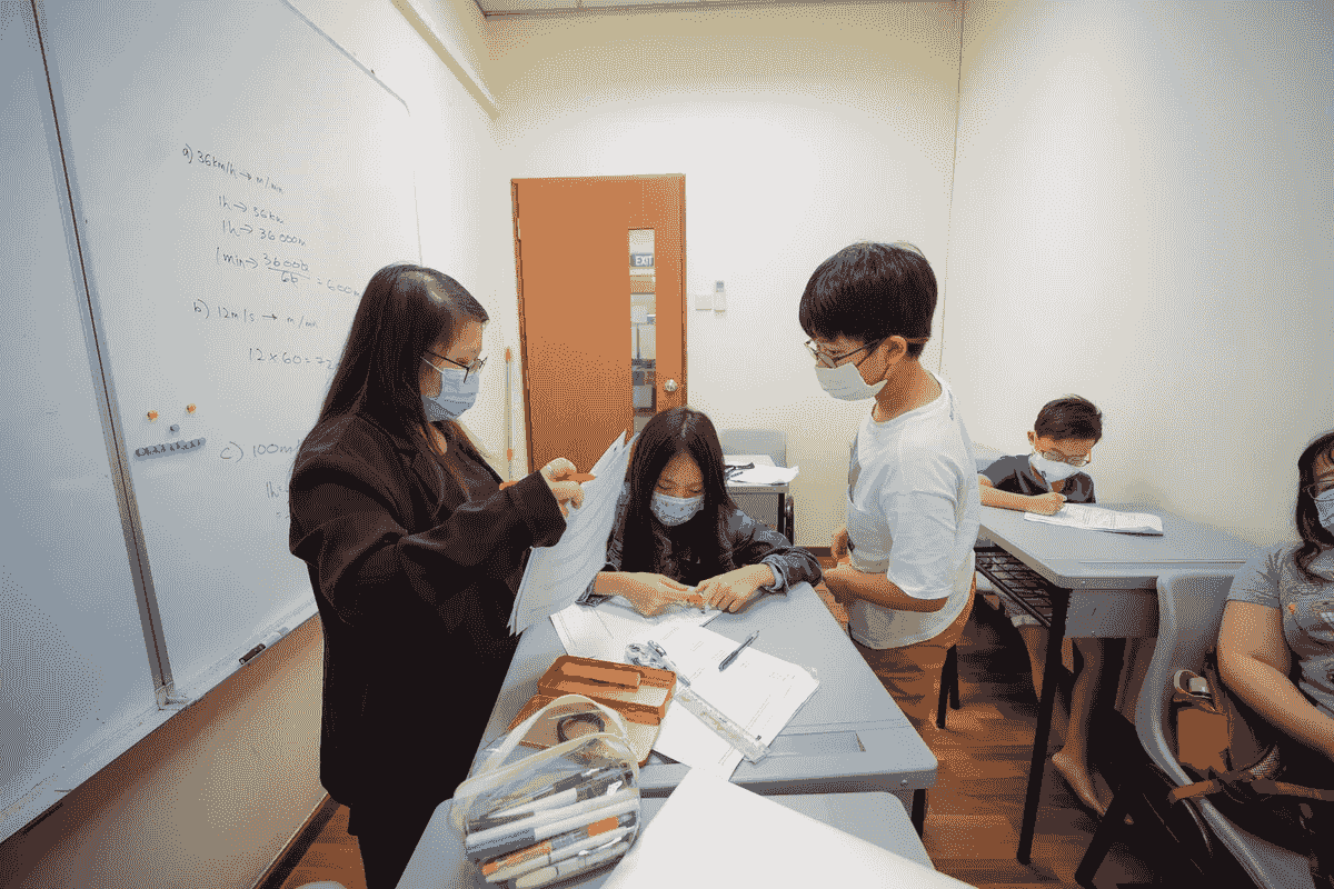 Math teacher assisting student with algebra problem at desk, personalized tutoring session in Singapore math tuition center focused on secondary school exam preparation Math teacher assisting student with algebra problem at desk, personalized tutoring session in Singapore math tuition center focused on secondary school exam preparation