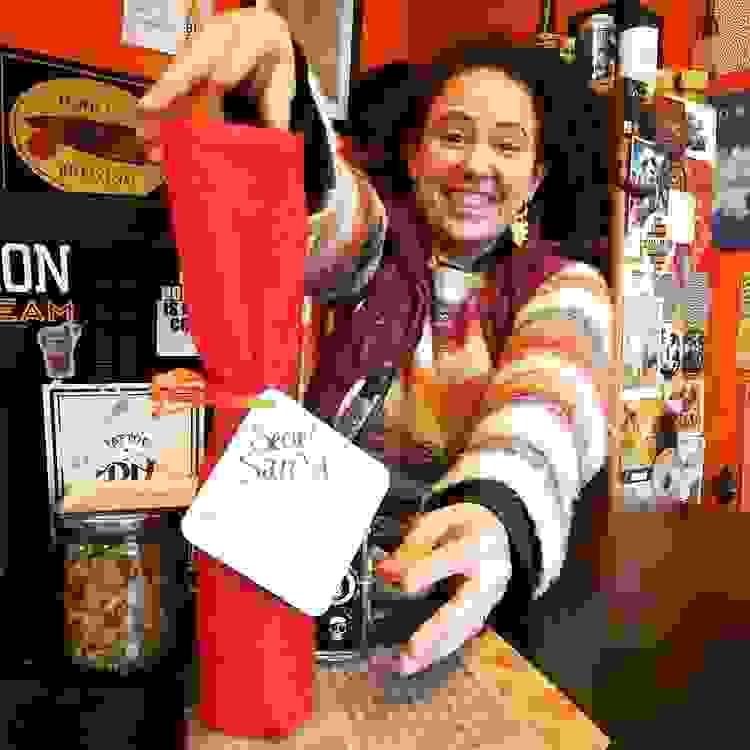 Jaclyn présentant une bouteille emballée sur le comptoir avec un petit mot accroché autour : Secret Santa. Remplacez-moi et emportez-moi ! Jaclyn présentant une bouteille emballée sur le comptoir avec un petit mot accroché autour : Secret Santa. Remplacez-moi et emportez-moi !